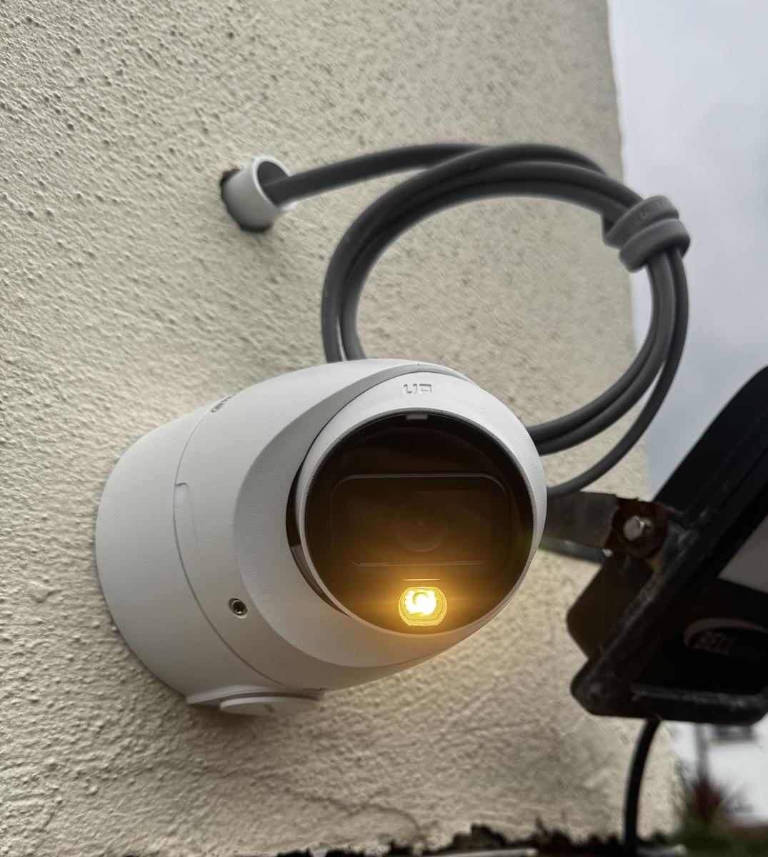 CCTV camera with its light on, mounted beside a floodlight